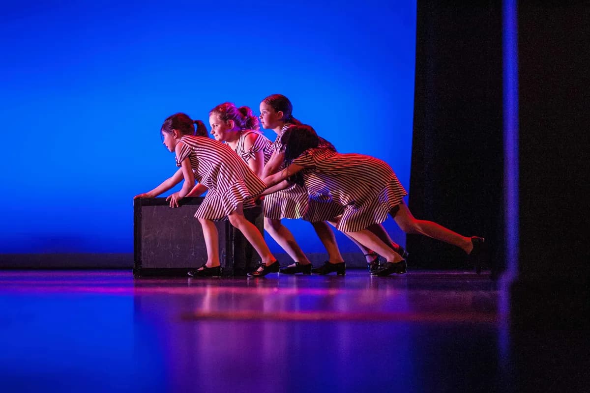 OVATION! dancers in striped costumes leaning over a trunk during a blue-lit Richmond Hill showcase