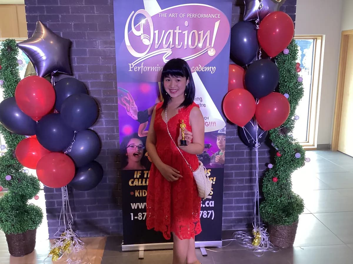 OVATION! student in a red dress holding her award between balloon towers at the That's A Wrap Film Fest in Richmond Hill
