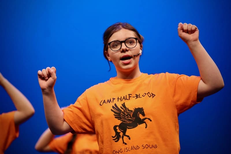 OVATION! summer musical production performer in a Camp Half-Blood t-shirt on a blue-lit Richmond Hill stage