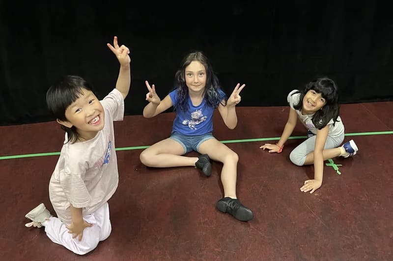 Three OVATION! KidsPlay campers flashing peace signs on the Richmond Hill studio floor