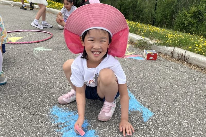 OVATION! KidsPlay camper in a sun hat drawing with sidewalk chalk during Richmond Hill outdoor playtime