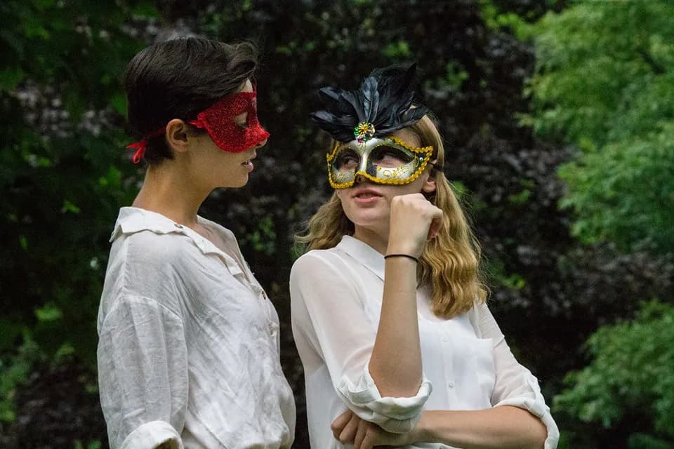 Two OVATION! performers in masquerade masks at an outdoor troupe performance